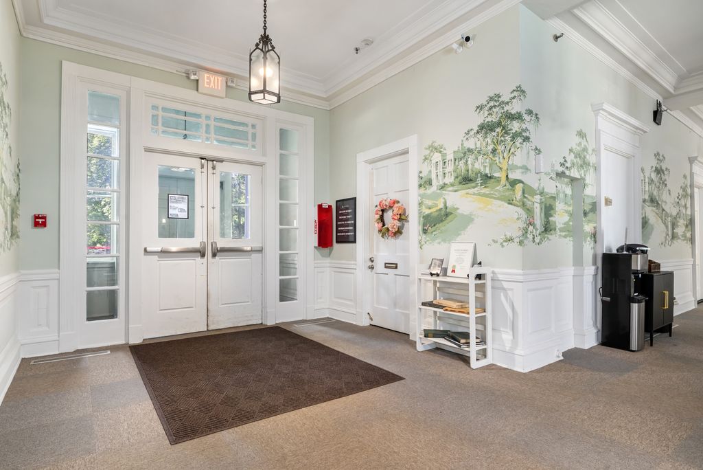 Lobby area with double glass doors, a brown doormat, a wall mural, a small cart with papers, a coffee maker, and decorative molding.