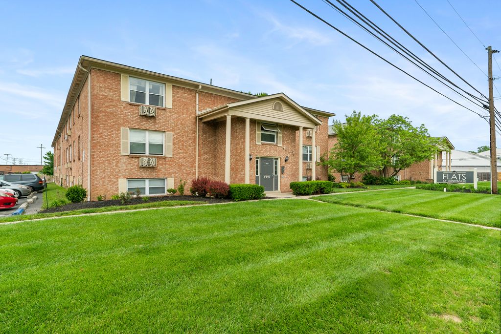 A two-story brick apartment building with columns at the entrance, surrounded by a neatly mowed lawn and some shrubs, under a clear blue sky.